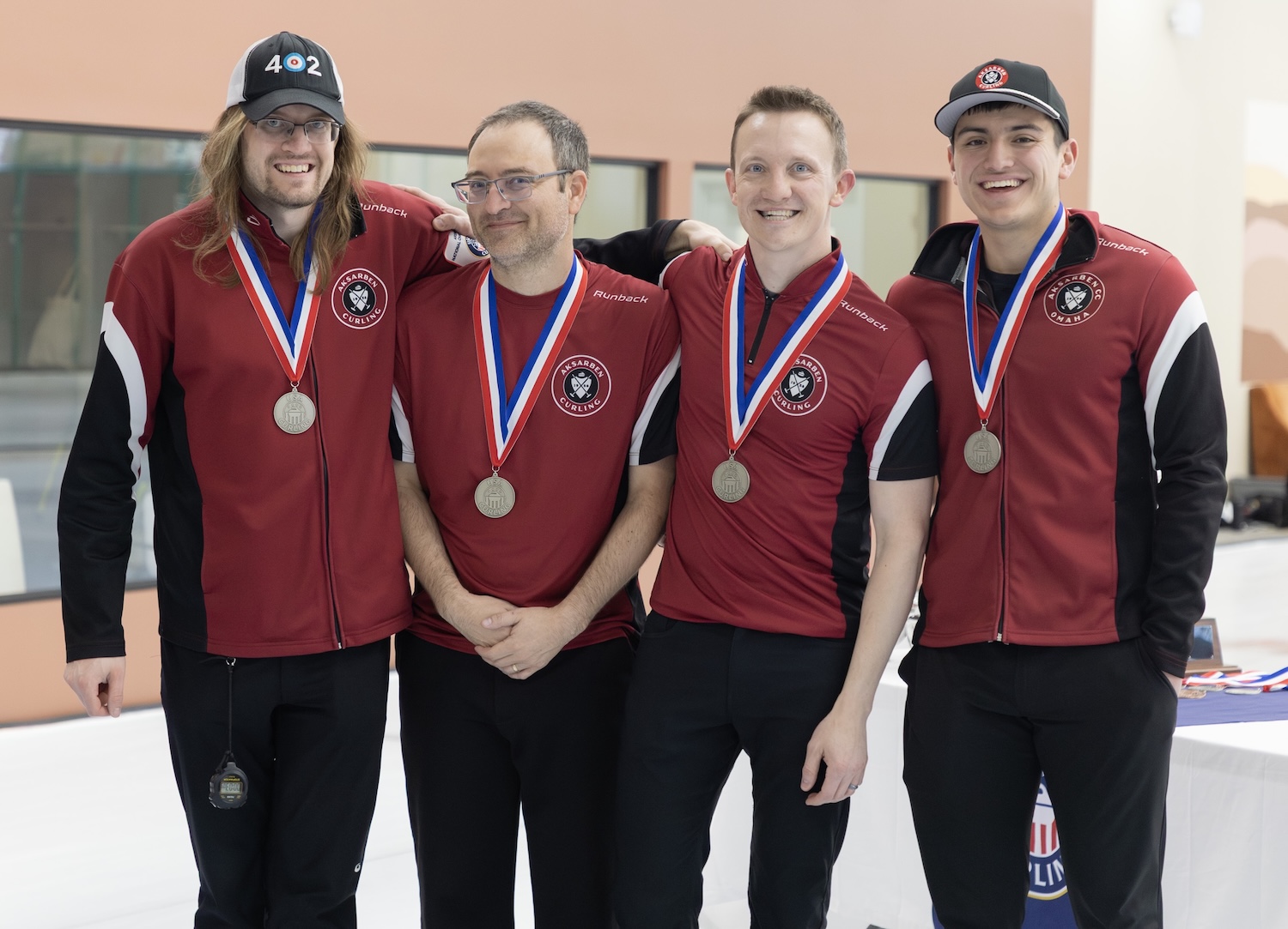 Four curlers wearing silver medals representing Aksarben Curling